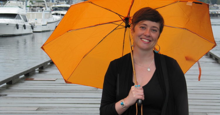 Heather Evans stands on a boat dock holding an orange umbrella.